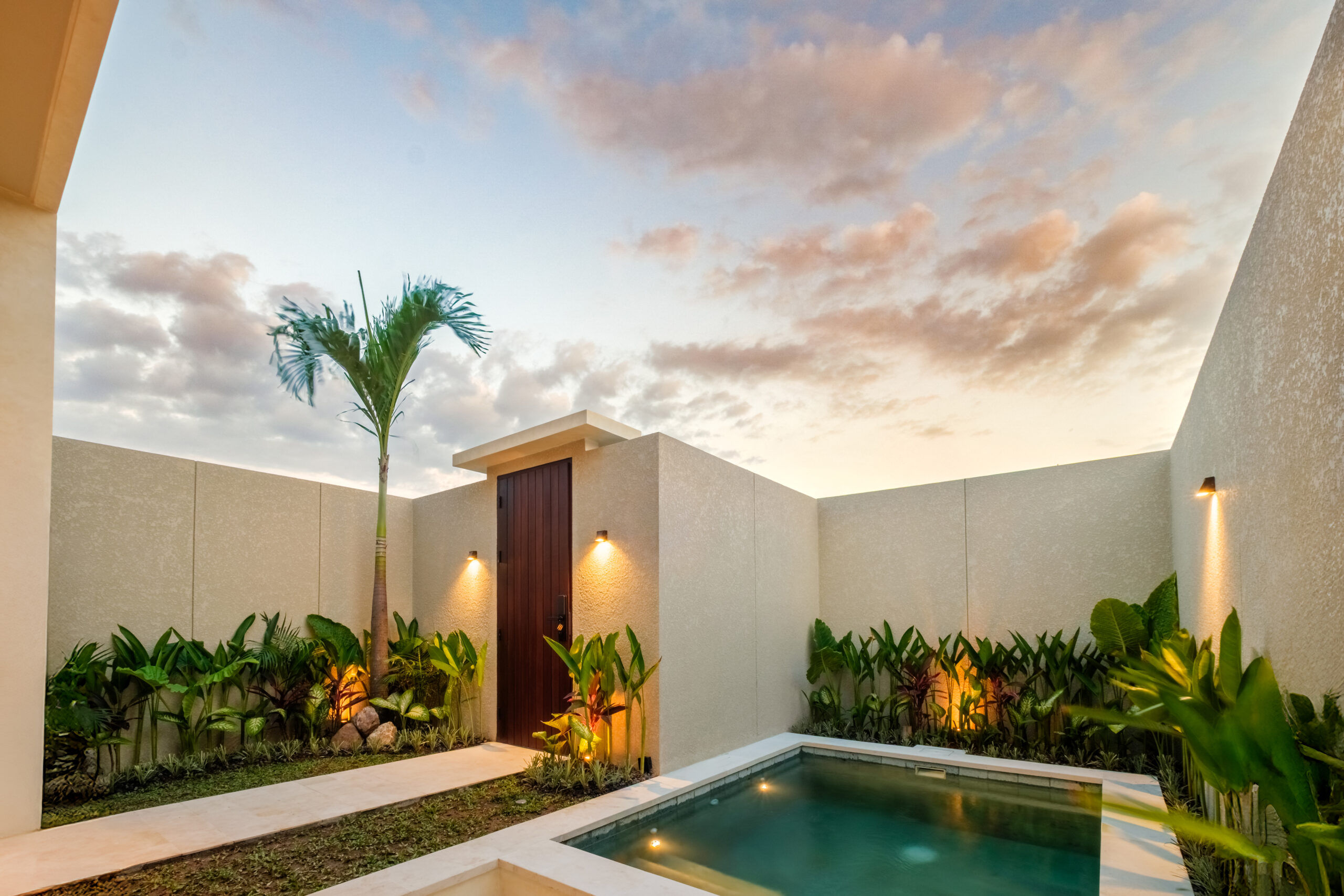 Lario Collection villa courtyard at dusk with a plunge pool, palm tree and timber door in Bali