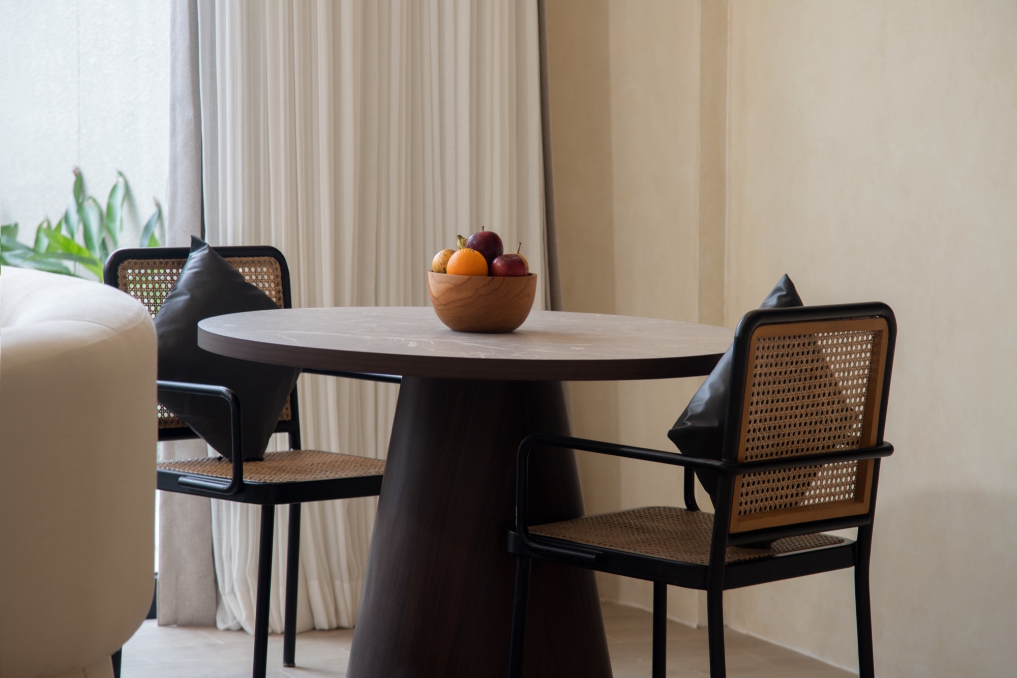 Round timber dining table with rattan-back chairs and a fruit bowl in a JSD Collective interior