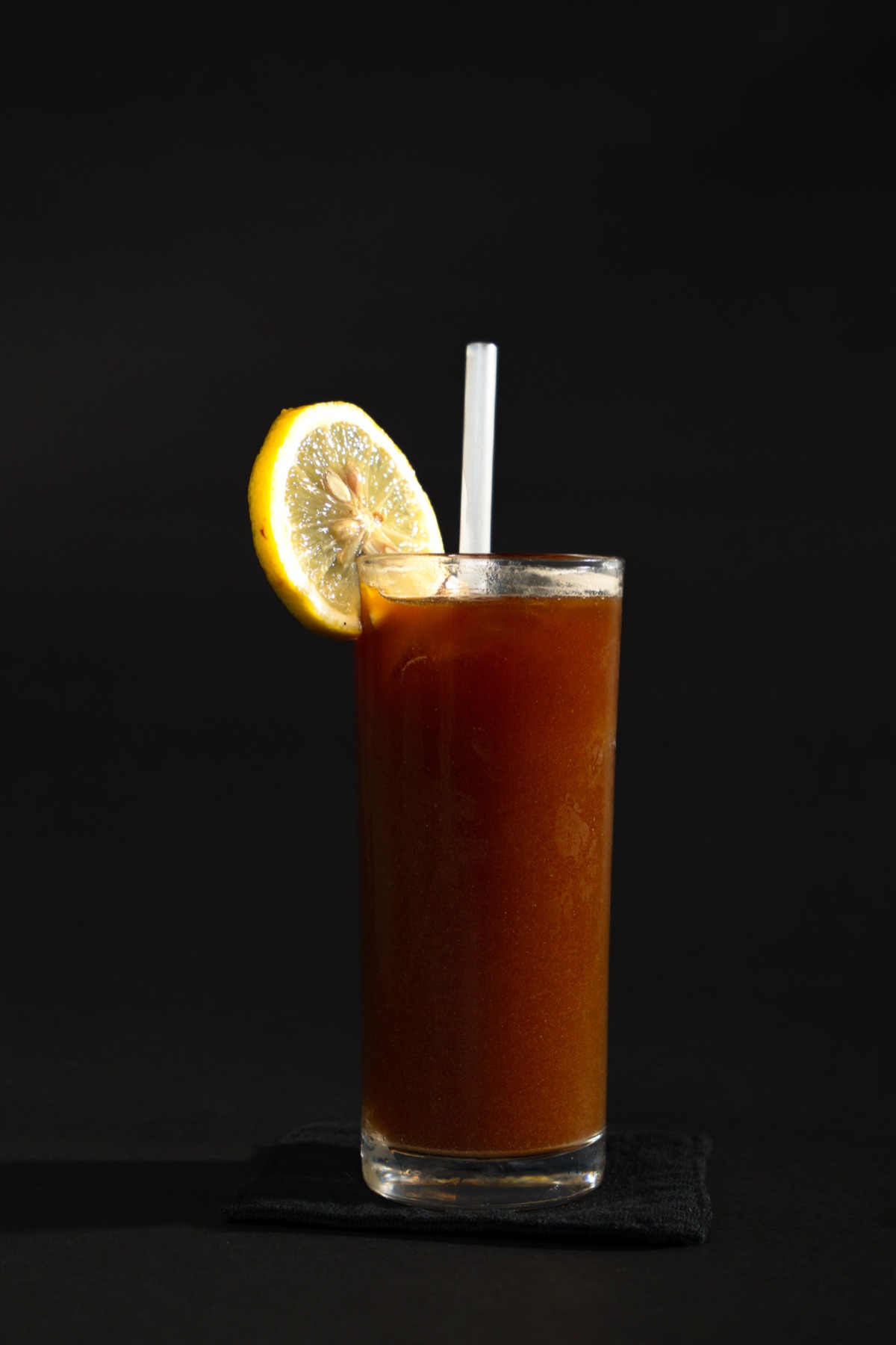 Tall iced coffee with a lemon slice and straw on a dark background