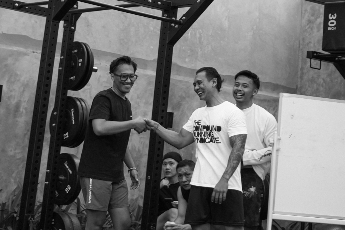 Black-and-white shot of members shaking hands by a squat rack at a Compound community event