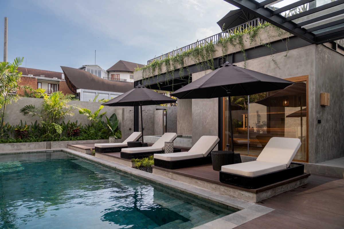 Pool terrace with white sun loungers and black umbrellas beside a concrete building