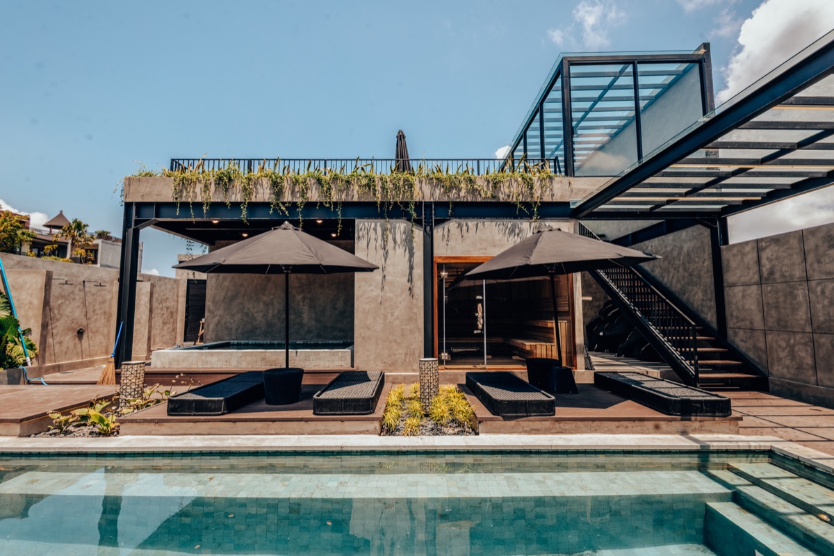 Pool deck with sun loungers, umbrellas and steel stairs up to a glass-railed rooftop
