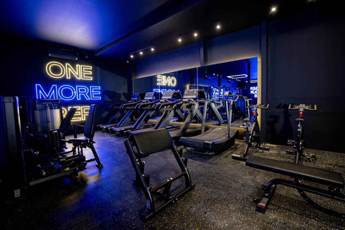 Found Wellness training floor with a weight bench, strength machines and treadmills under neon light