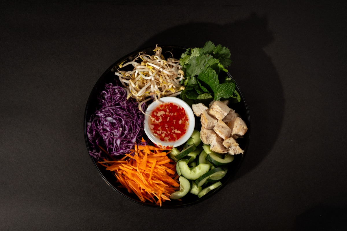 Wholefood bowl of chicken, cucumber, carrot, red cabbage, bean sprouts and herbs with chilli dip