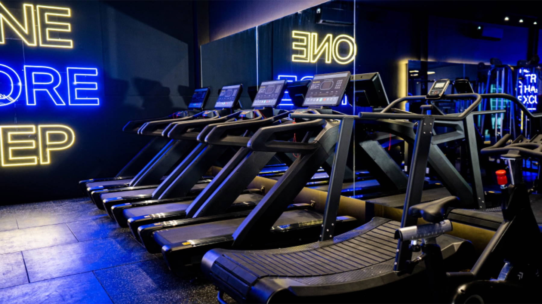 Row of curved manual treadmills under neon "One More Rep" signs at Found Wellness