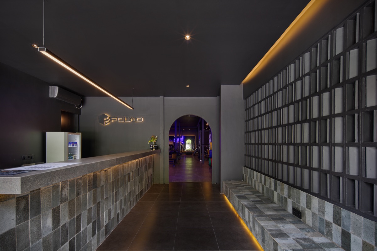 Found Wellness reception with a tiled counter, glass-block wall and arched doorway to the gym