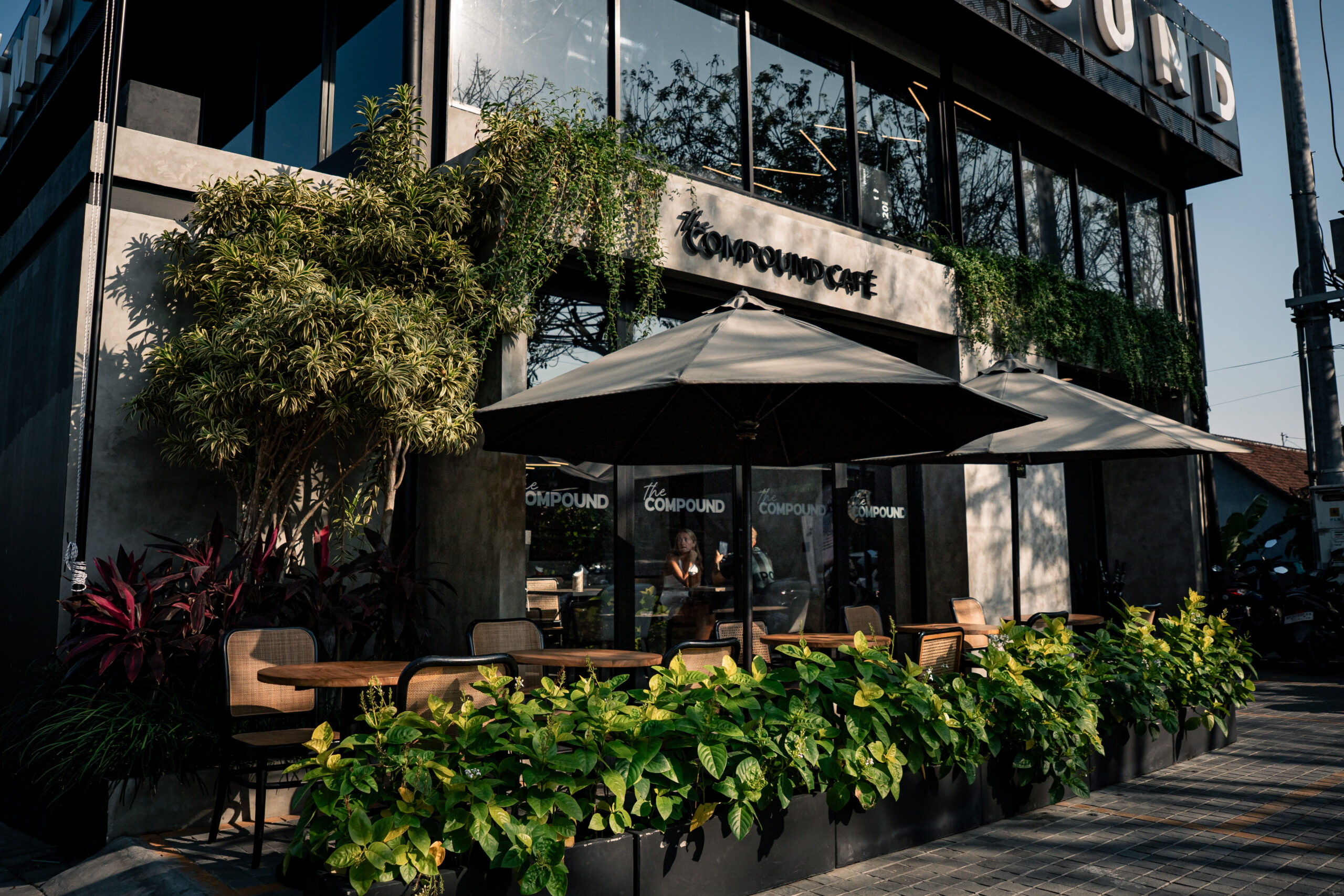 Compound Cafe's plant-lined alfresco terrace with umbrellas and outdoor tables